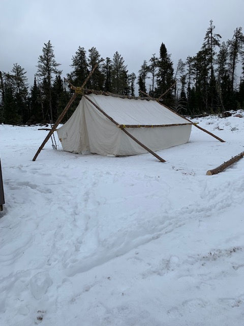 A tipi sitting on a snow bank at Bug Lake camp
