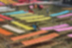 People hang up long sheets of brightly coloured fabric in a field