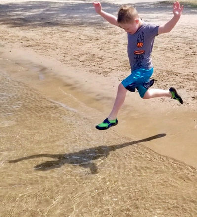 Riley in midair with arms spanning out to the side as he is about to run into the water. His shadow looks like a bird with its wings spread.