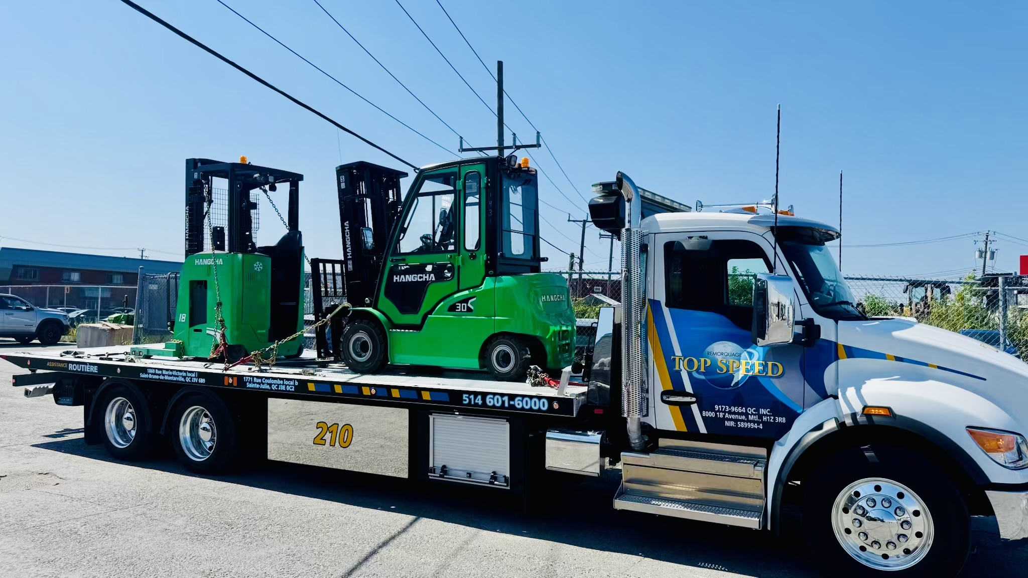 Deux chariots élévateurs verts arrimés sur le plateau d’un camion.