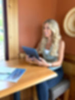 Smiling woman sitting at a wooden table in a cozy café, holding a tablet with printed documents and a pen beside her