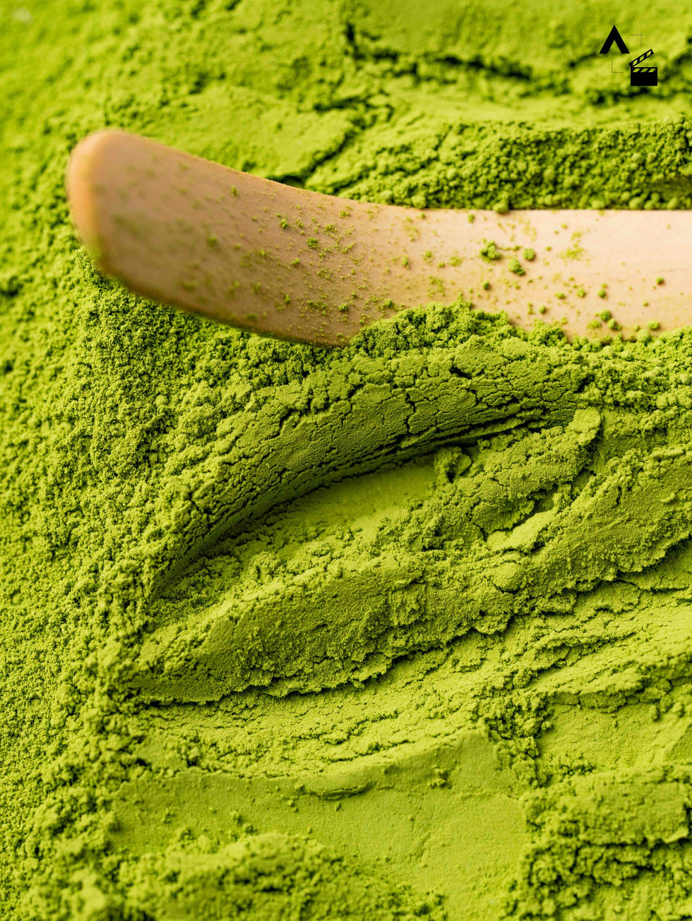 Macro texture shot of vibrant, bright green organic ceremonial matcha powder being smoothed over by a light wooden chashaku spoon.