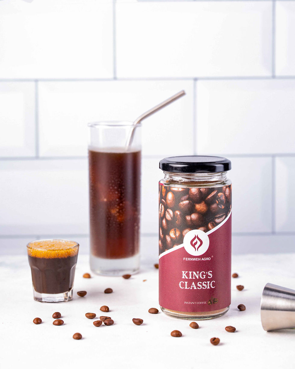 A minimalist, bright product shot of a Fernweh Agro King's Classic instant coffee jar sitting on a clean white tiled background next to a tall glass filled with chilled black iced coffee and a metal straw.