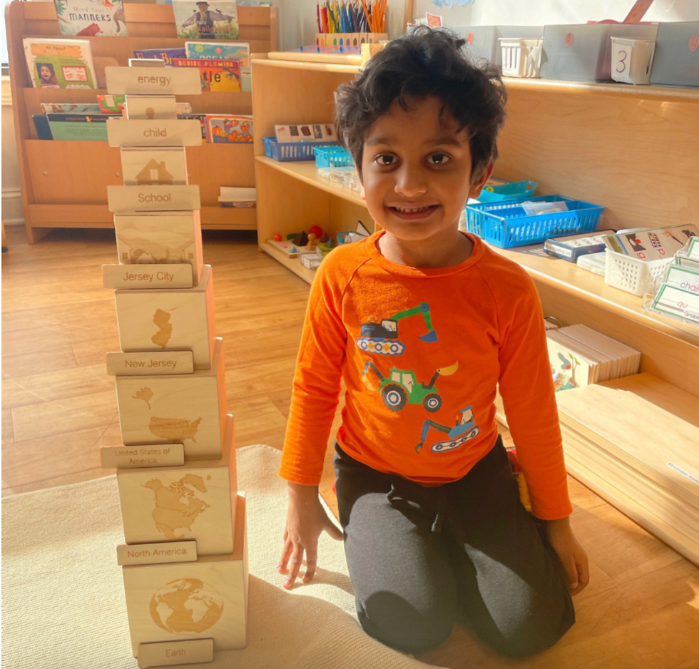 Child smiling next to Montessori Cosmic Nesting Boxes