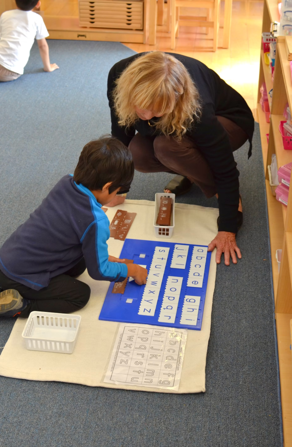 Montessori teacher guides a student in matching lowercase letters with picture cards to strengthen phonics, letter recognition, and early reading skills.