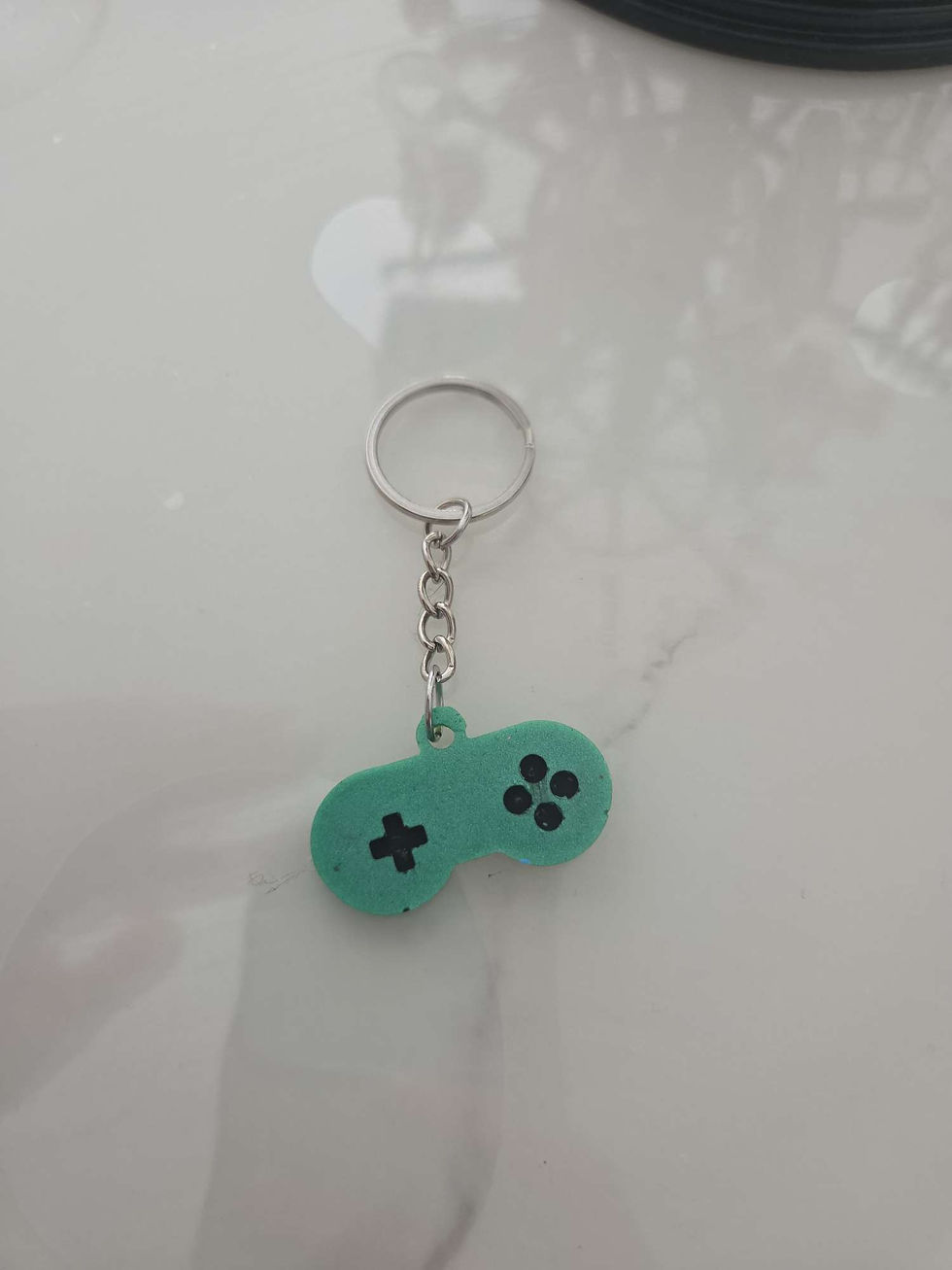 Porte-clés vert en forme de manette de jeu sur fond clair.