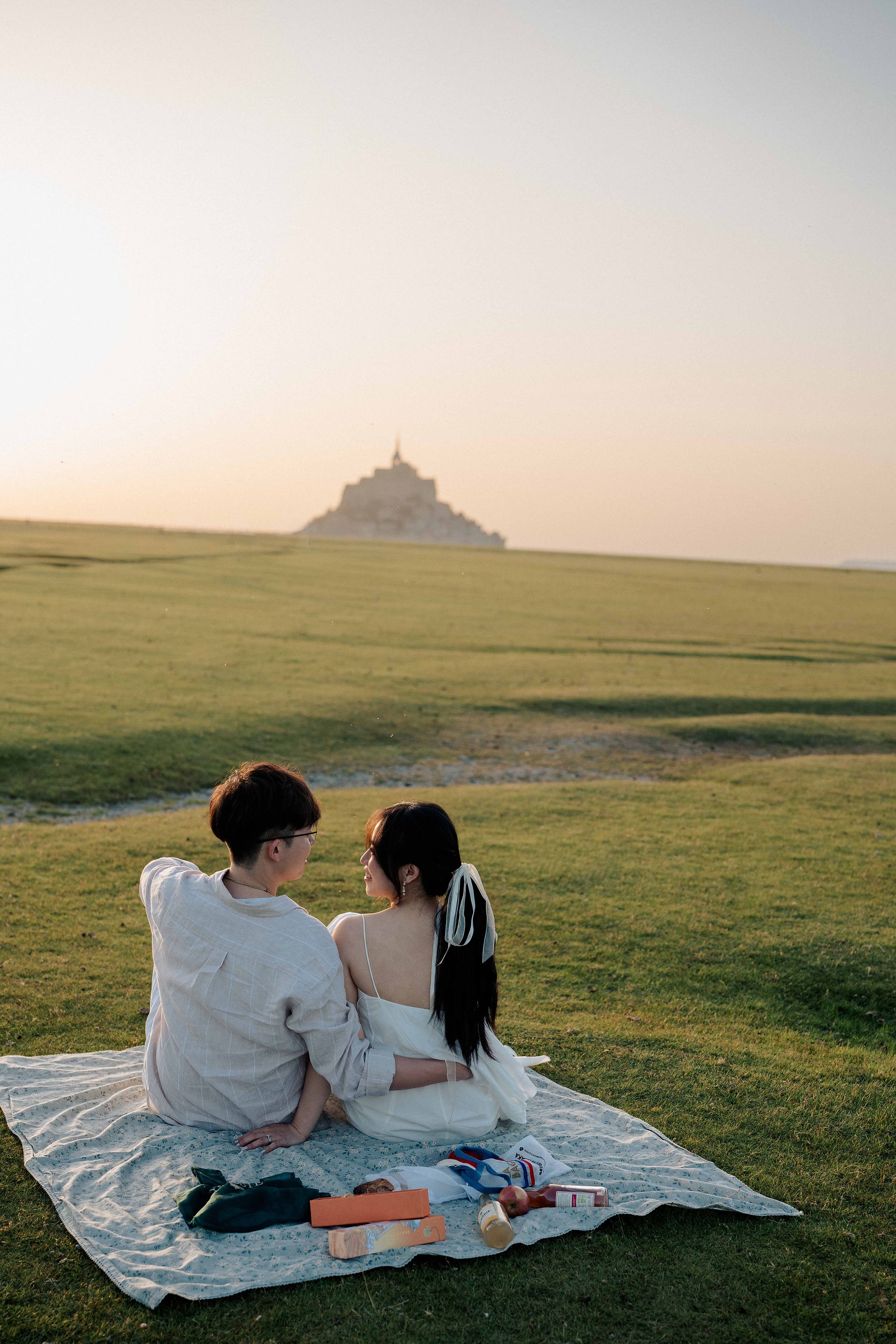 Couple sitting on a picnic blanket looking towards Mont Saint-Michel at sunset