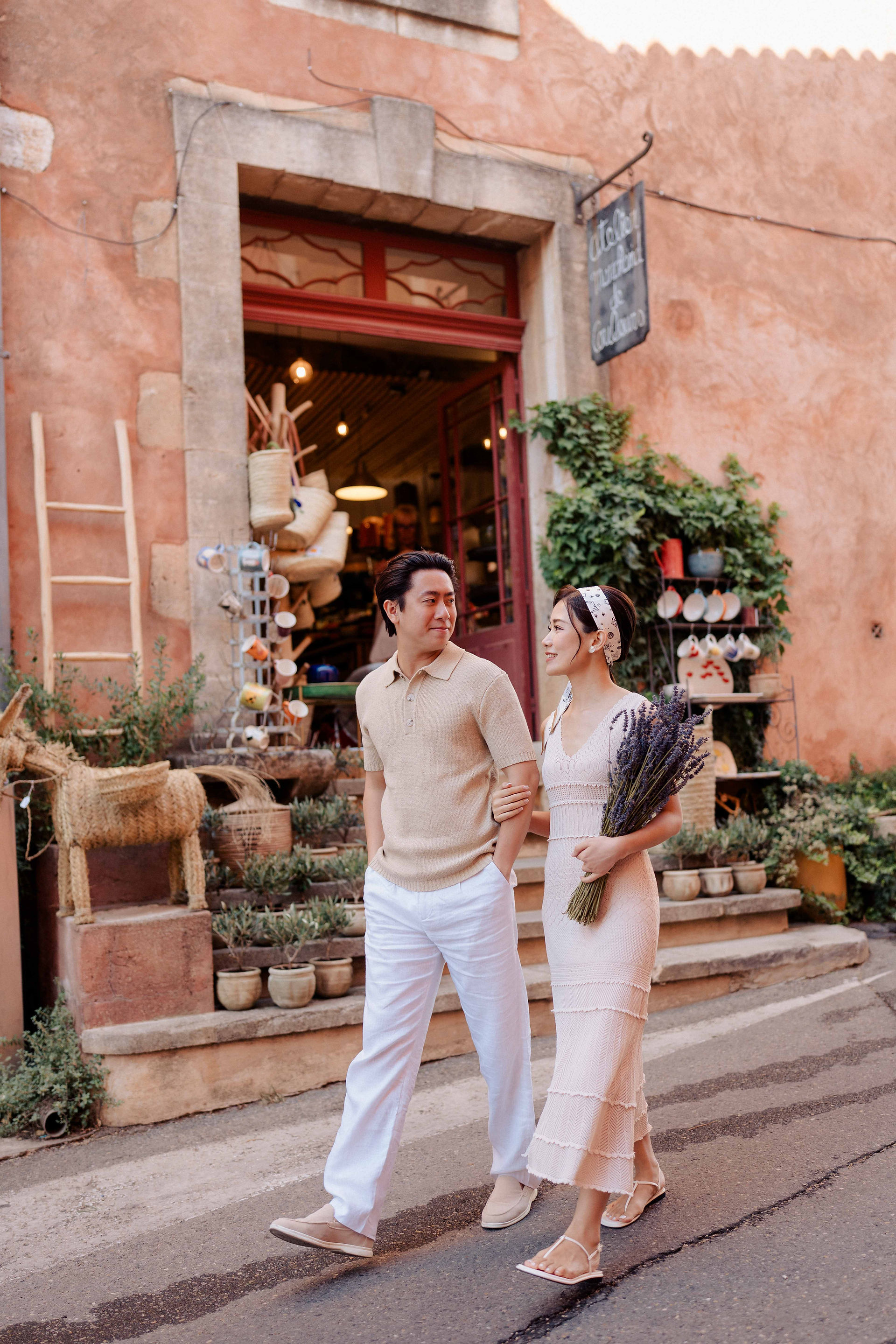 Couple walking together in middle of Roussillon village passing in front of a flower shop and holding a lavender bouquet