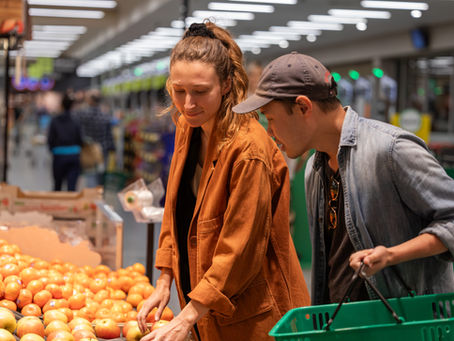 Shoppers carefully select fresh produce in a vibrant grocery store setting.