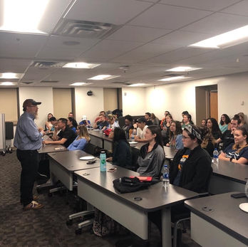 University professor teaching a classroom of Event Management students, discussing famous festival failures and real-world lessons in crisis management.