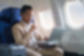 Elegant businessman using laptop while sitting in airplane cabin with sun shining trough a