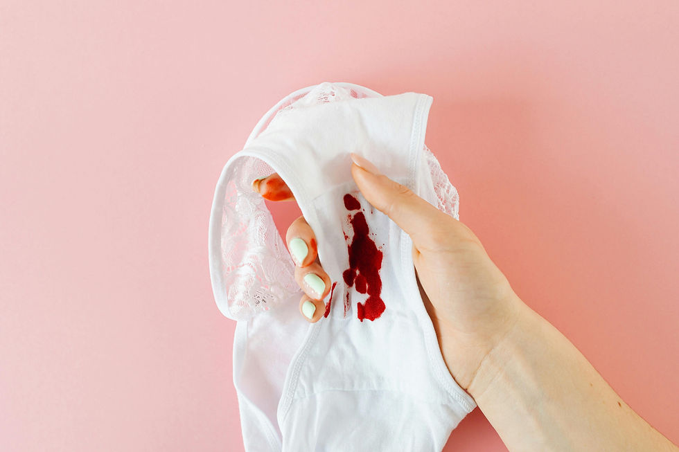 Hand holding white underwear with menstrual blood stain on pink background, symbolizing free bleeding and conscious menstrual management.
