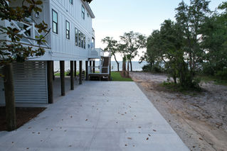 a white house with a concrete driveway leading to the beach