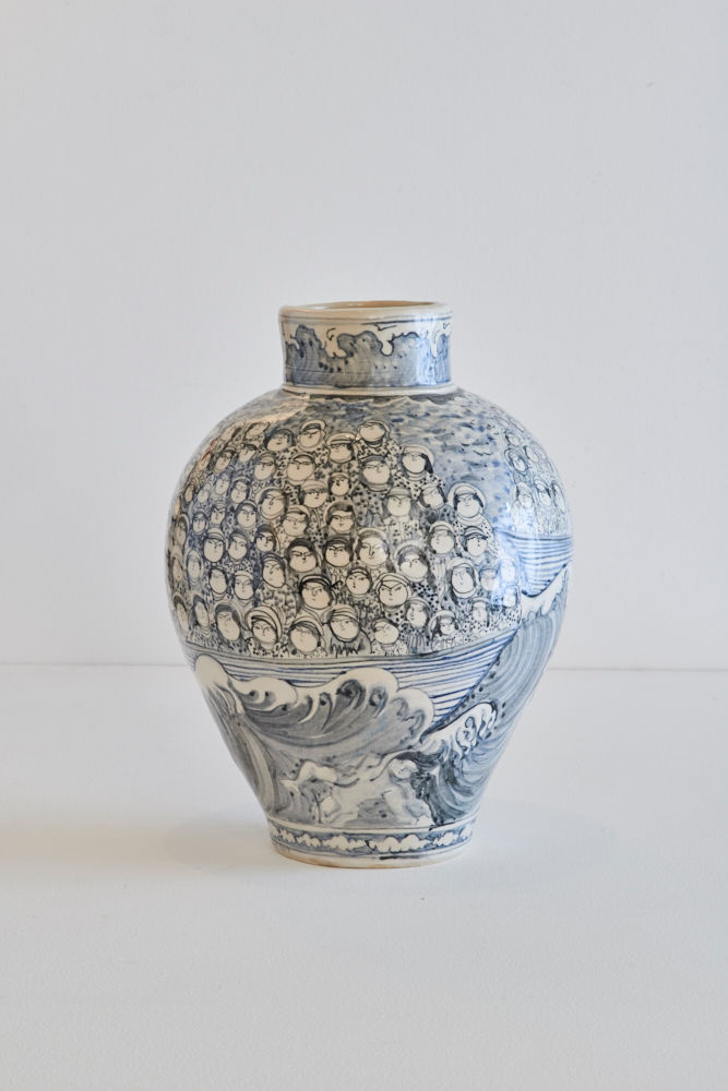 You see a vase, where you see heads of many people, on the right side a boat, people sitting in. The bottom of the vase show big waves.