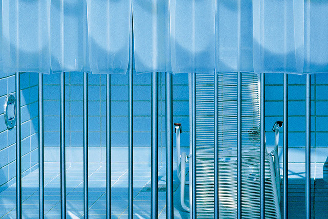 Hinter Gittern sieht man einen Liegestuhl auf dem Grund eines Münchner Freibads vor blauen Fließen. Das Becken ist ohne Wasser.