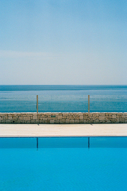 Der Ausschnitt eines Hotelpools in Italien, der direkt am Meer liegt. Man sieht über die Wasserfläche hinaus auf den Horizont des Meeres.