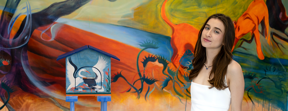 Michelle Foley posing with her senior thesis project, a birdhouse and a mural.