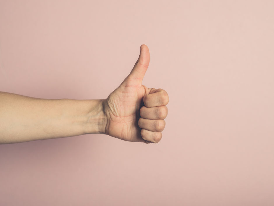 A hand gives a thumbs-up against a light pink background, conveying positivity and approval.