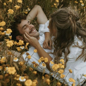 Cette image représente un couple amoureux en train de s’embrasser dans un champs de fleurs.
