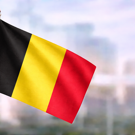 Belgian flag in black, yellow and red captured in close-up, waving against a softly blurred urban backdrop.