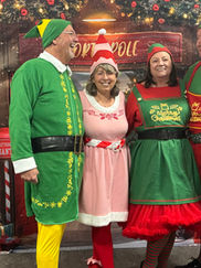 A woman in a black dress and a man in a tuxedo posing together in front of a Christmas-themed backdrop