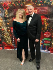 A woman in a green velvet dress and a man in a black tuxedo standing together in front of a festive backdrop