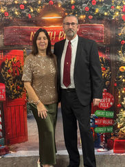 A woman in a shimmering gold dress and a man in a tuxedo posing in front of a festive "North Pole" display