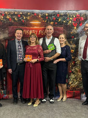 A group of eight people, dressed formally, stand smiling in front of a festive