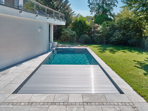 Unterflur Rollladen auf Veltmann Schwimmbad in der Sonne architektonisch eingearbeitet in schöne grau glänzende Steine in gepflegter Rasenfläche