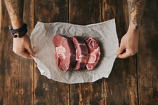 top-view-tattooed-hands-hold-white-craft-paper-with-three-raw-great-leg-steaks-with-bone-i
