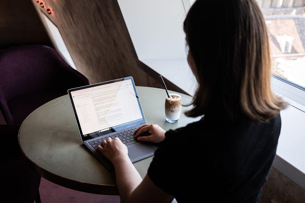 A brown-haired woman turned back writing on a laptop with iced coffee