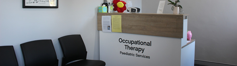 Our waiting room with black chairs on the left, frames with children's drawings and inspirational quotes on all walls, a white and brown front desk with colourful children's toys on the right wall.