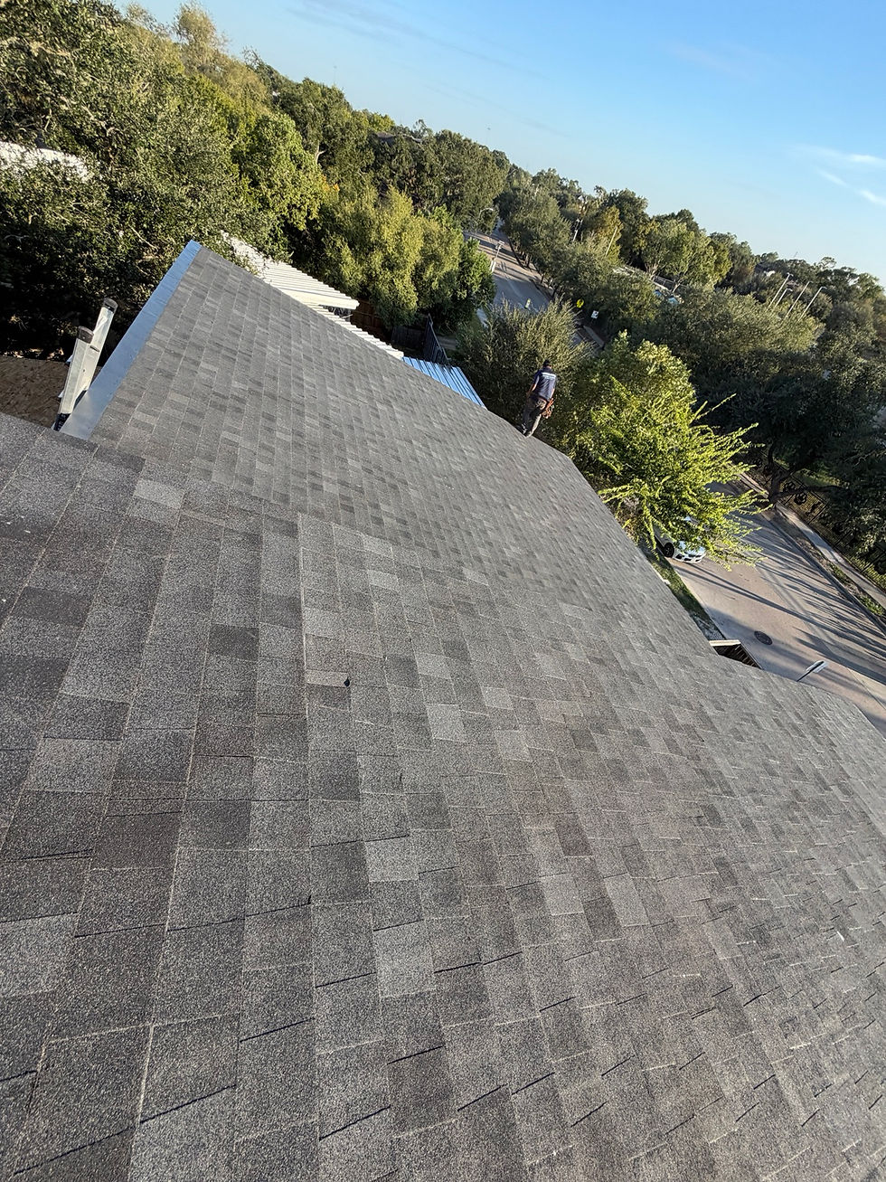Dark shingles across a roof slope with a crew member near the far edge.