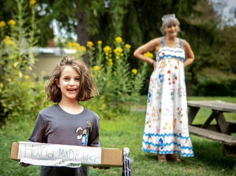 Child holding a welcome sign on the lawn at the Bluefield Farm celebration, with family nearby.