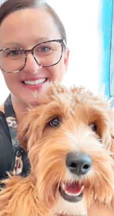 Stella smiling beside a freshly groomed doodle in a calm, one-on-one environment