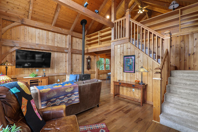 Great room with timber frame beams, wood stove, hardwood floors, and large windows in an Oregon mountain acreage home.