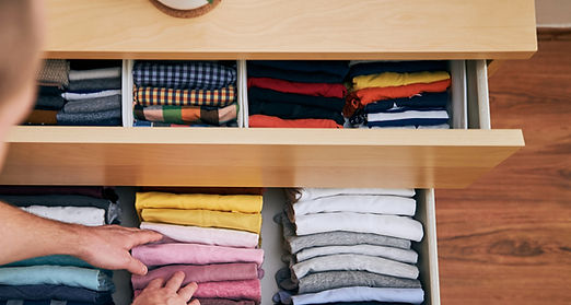 Organizing and cleaning home. Man preparing orderly folded t-shirts in drawer with his cur