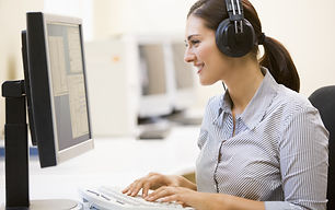 Woman typing on a computer with a headset on.