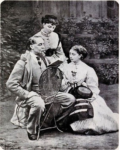 Imagem antiga em preto e branco de u homem sentado lendo um livro com duas mulheres ao lado