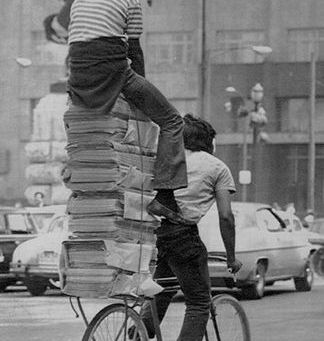 Foto antiga de dois garotos e uma pilha de papéis em uma bicicleta