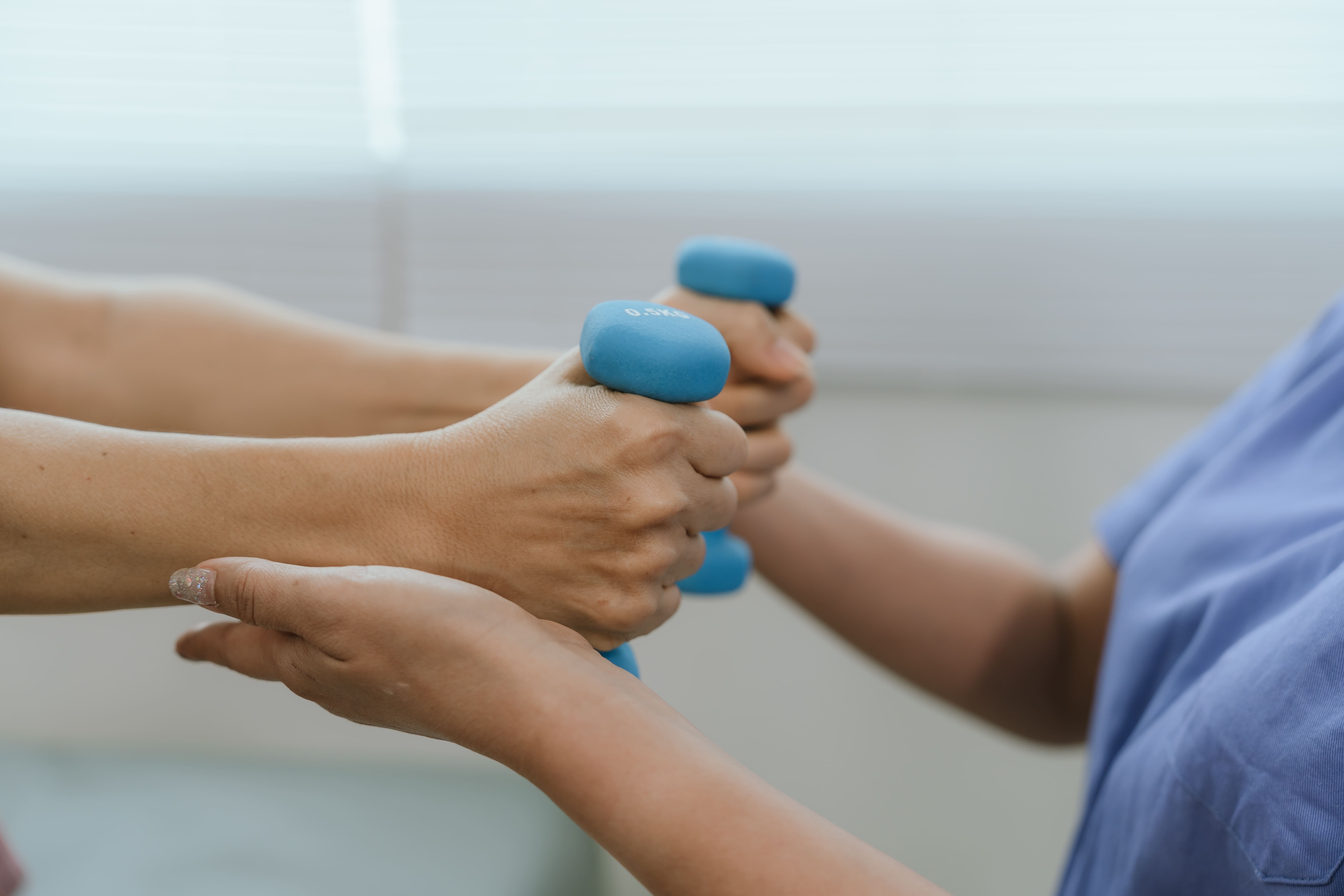 Senior woman exercising with dumbbells during physical therapy in hospital. Physiotherapist helps promote strength, mobility and healthy living.