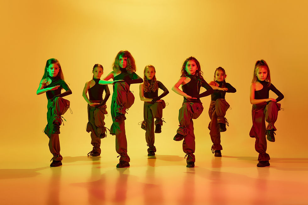 Danse de l'émotion, hip-hop. Groupe d'enfants, petites filles en vêtements sportifs élégants dansant sur fond studio jaune à la lumière du néon. Concept d'enfance, de loisir, de vie sportive, d'art
