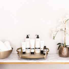 Image of white orchids displayed with skincare products and rolled up spa towels in a gold bowel.