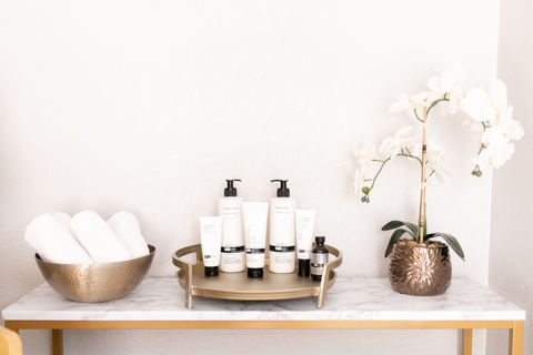 Image of white orchids displayed with skincare products and rolled up spa towels in a gold bowel.
