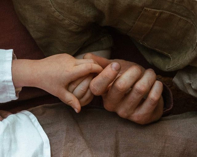 Mains d'un enfant et d'un adulte se tenant tendrement. Fond brun et beige, symbolisant la connexion et l'affection.