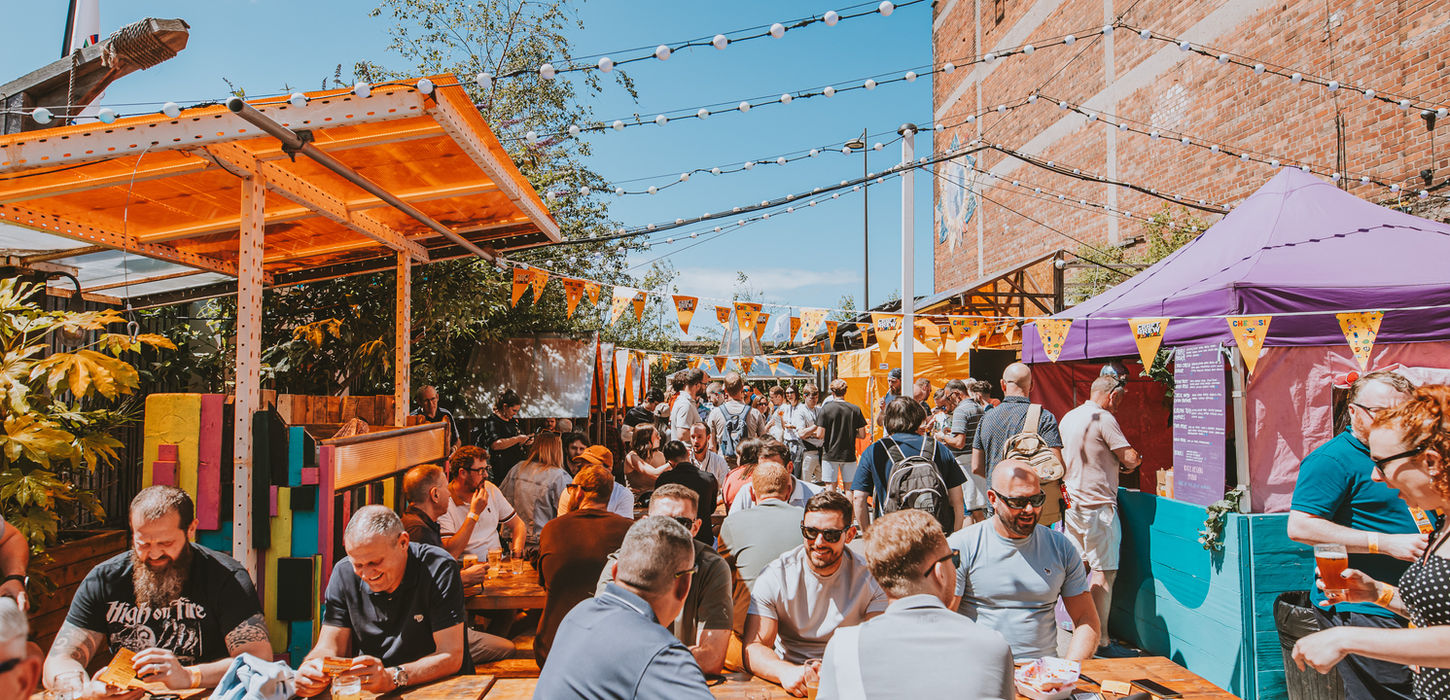 Outdoor crowd gathered at tables with drinks on a sunny day.
