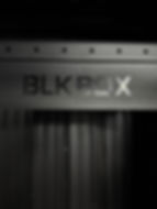 Black metal with the cutout text "BLK BOX," featuring a modern, minimalist design against a dark, industrial backdrop