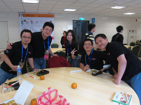 一群人在圓桌旁合影,微笑,比勝利手勢,穿著黑色上衣和牛仔褲