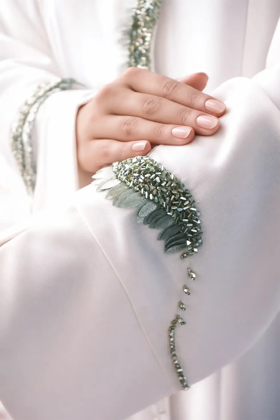 Close-up of sage green fabric petals and emerald green beads on the sleeve of a luxury ivory abaya.