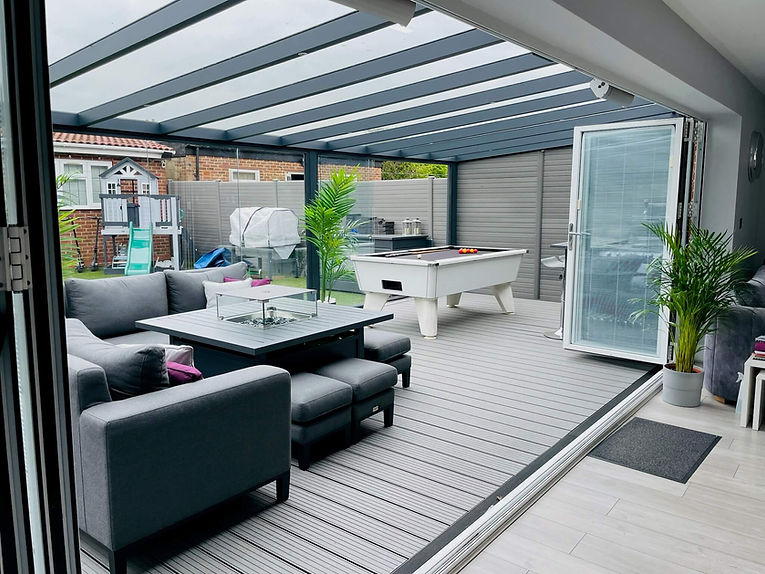Anthracite grey glass room veranda with a glass roof, furnished with a grey garden sofa and table, including a white pool table.